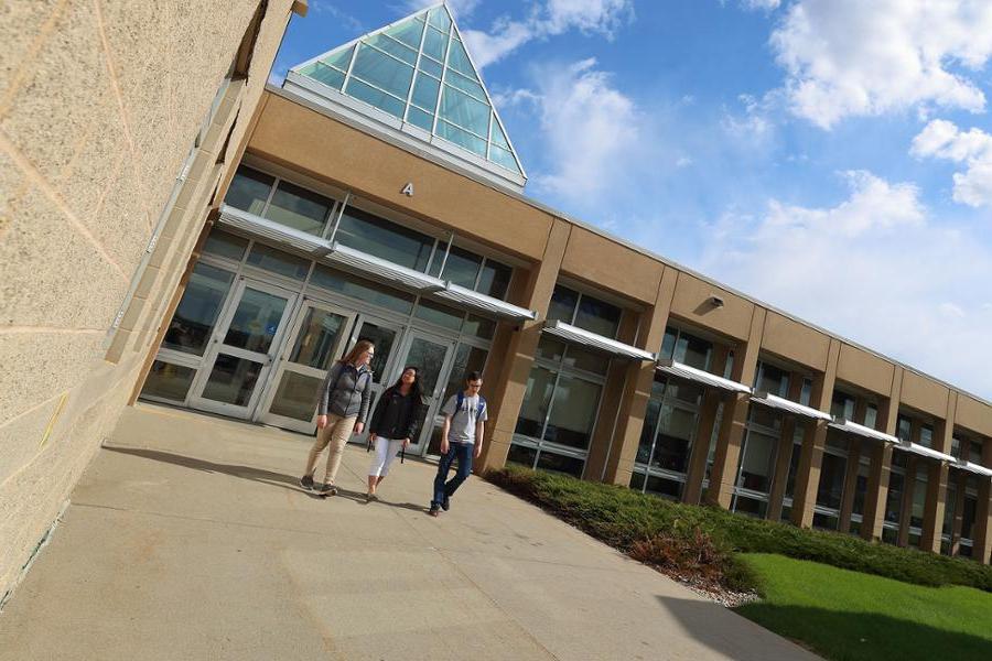 Three students walking out of health building on sunny day